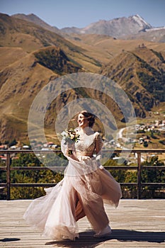 Beautiful bride in a nice dress stands on the terasse with great mountain view in Georgia