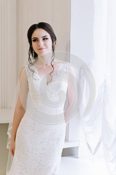 Beautiful bride perfect style. Wedding hairstyle make-up dress and bride`s bouquet. Young attractive bride near window in white r