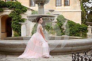 Beautiful bride in pink prom dress by round fountain. Outdoor romantic portrait  of Attractive brunette woman with makeup and