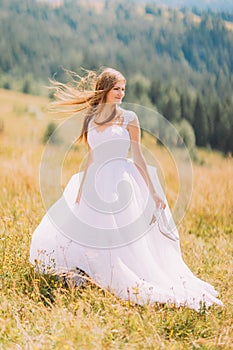 Beautiful bride posing on the golden autumn field with astonishing mountain landscape behind her