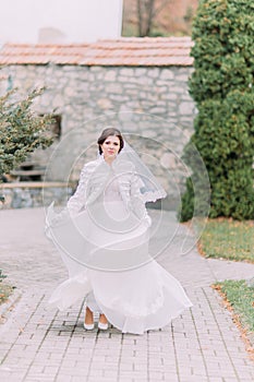 Beautiful bride posing in green sunny park waving her elegant wedding dress