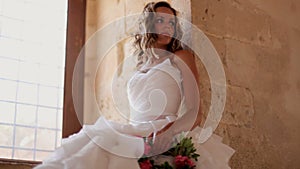 A beautiful bride sits near a window in an old castle