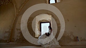 A beautiful bride sits near a window in an old castle