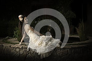 Beautiful bride in strapless vintage wedding dress reclining next to a courtyard fountain photo