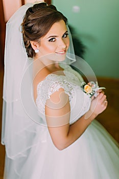 Beautiful bride with stylish make-up in white dress posing, holding cute little boutenniere