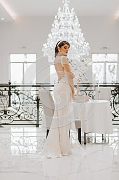 Beautiful bride at the table with a vase of flowers. The woman is wearing a long wedding dress with lace and an open back