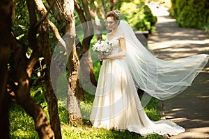 Beautiful bride walking in the park. Wedding veil disperse of wind. Beauty portrait of a bride around amazing nature