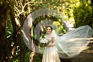 Beautiful bride walking in the park. Wedding veil disperse of wind. Beauty portrait of a bride around amazing nature