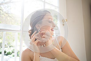 Beautiful bride wearing earring while standing by window