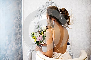 A beautiful bride with a wedding bouquet in her hands sits in a chair, back view.