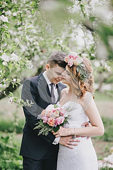 Beautiful bride in a wedding dress with bouquet and roses wreath posing with groom wearing wedding suit