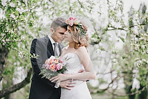 Beautiful bride in a wedding dress with bouquet and roses wreath posing with groom wearing wedding suit