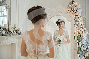 Beautiful bride in a wedding dress at a mirror in Christmas. Girl repeats the hairstyle and makeup.
