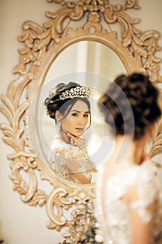 Beautiful bride in a wedding dress at a mirror in Christmas. Girl repeats the hairstyle and makeup.