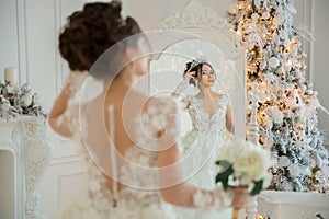 Beautiful bride in a wedding dress at a mirror in Christmas. Girl repeats the hairstyle and makeup.