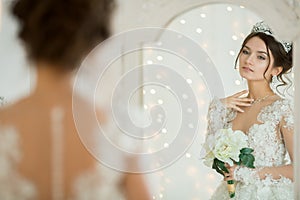 Beautiful bride in a wedding dress at a mirror in Christmas. Girl repeats the hairstyle and makeup.