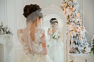 Beautiful bride in a wedding dress at a mirror in Christmas. Girl repeats the hairstyle and makeup.