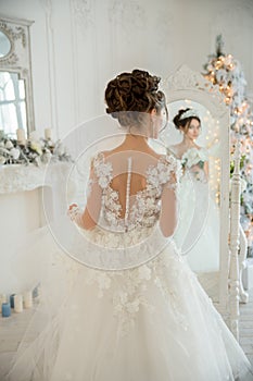 Beautiful bride in a wedding dress at a mirror in Christmas. Girl repeats the hairstyle and makeup.