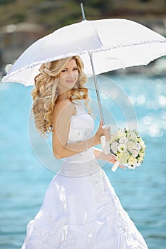 Beautiful bride in wedding dress with white umbrella and bouquet