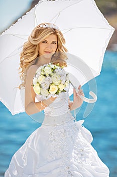 Beautiful bride in wedding dress with white umbrella and bouquet