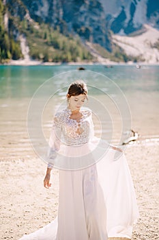 Beautiful bride in a white chiffon dress with sleeves and lace on the shore of Lake Lago di Braies in Italy. Destination