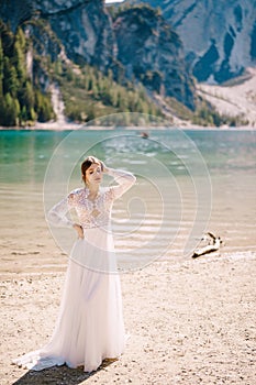 Beautiful bride in a white chiffon dress with sleeves and lace on the shore of Lake Lago di Braies in Italy. Destination