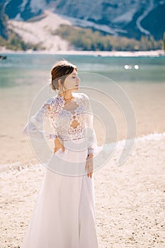 Beautiful bride in a white chiffon dress with sleeves and lace on the shore of Lake Lago di Braies in Italy. Destination