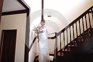 Beautiful bride in a white dress with a bouquet of flowers in her hands goes down the stairs