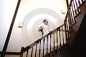 Beautiful bride in a white dress with a bouquet of flowers in her hands goes down the stairs