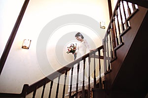 Beautiful bride in a white dress with a bouquet of flowers in her hands goes down the stairs