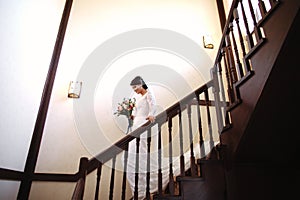 Beautiful bride in a white dress with a bouquet of flowers in her hands goes down the stairs