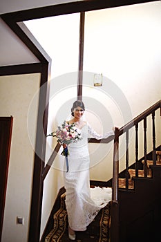 Beautiful bride in a white dress with a bouquet of flowers in her hands goes down the stairs