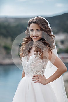 Beautiful bride in white dress posing on sea and mountains in background