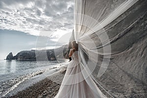 Beautiful bride in white dress posing on sea and mountains in background