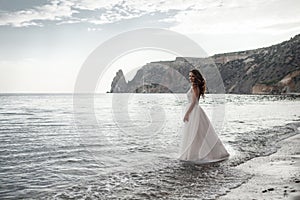 Beautiful bride in white dress posing on sea and mountains in background