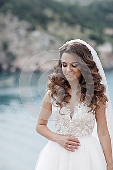 Beautiful bride in white dress posing on sea and mountains in background