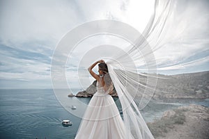 Beautiful bride in white dress posing on sea and mountains in background