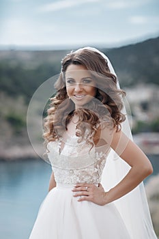 Beautiful bride in white dress posing on sea and mountains in background