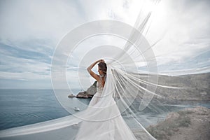 Beautiful bride in white dress posing on sea and mountains in background