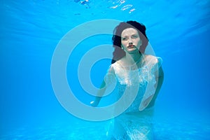 Beautiful bride in white dress posing underwater at the bottom of the pool on a Sunny day. Unusual wedding. Fashion