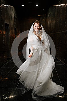 beautiful bride in a white elegant dress, with a veil goes down a dark corridor