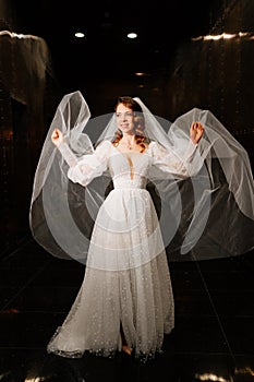 beautiful bride in a white elegant dress, with a veil goes down a dark corridor