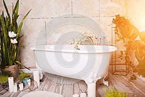 Beautiful bright bathroom with large white bath, green flowers, candles