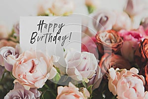 bright bouquet of colorful roses with white card with the inscription happy birthday, concept of congratulations