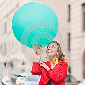 Beautiful bright girl on a city street lifestyles with green balloons smiling and posing in a red suit