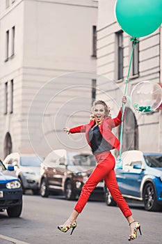 Beautiful bright girl on a city street lifestyles with green balloons smiling and posing in a red suit