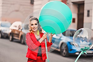 Beautiful bright girl on a city street lifestyles with green balloons smiling and posing in a red suit