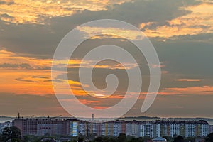 Beautiful bright orange sky at sunset over high apartment building, working tower cranes and houses roofs among green trees on di