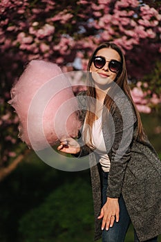 Beautiful brown hair model hold a cotton candy in hands and give a kiss. Young woman with pink cotton candy