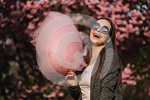 Beautiful brown hair model hold a cotton candy in hands and give a kiss. Young woman with pink cotton candy